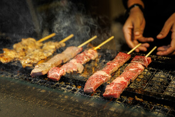 Raw and cooked meat skewers grilling over charcoal