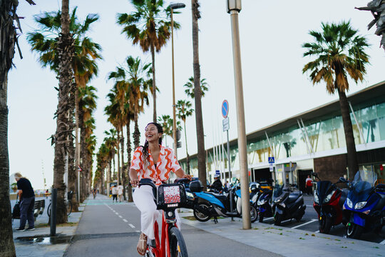 Smiling young Black woman riding red rental bike, embracing digital mobility and independence, showing balance of technology, personal freedom and joyful energy in modern city life.