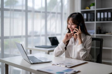 Asian businesswoman talking on smartphone and working with laptop in office