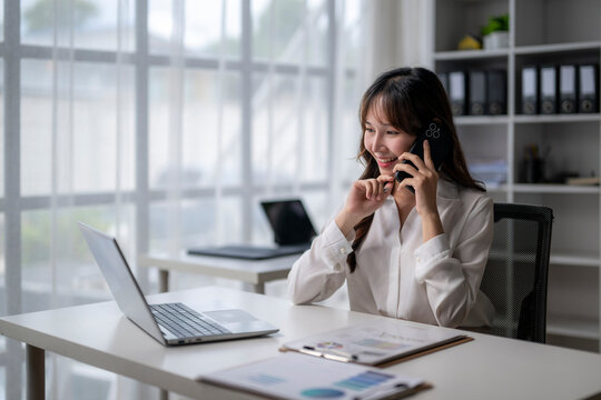 Asian businesswoman talking on smartphone and working with laptop in office