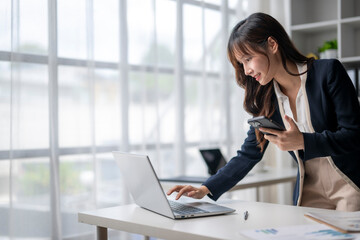 Businesswoman working on laptop and holding smartphone in office