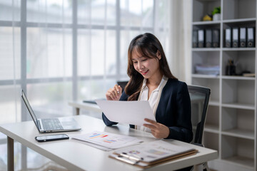 Smiling asian businesswoman reviewing documents and working with financial charts at desk in office