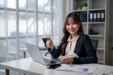 Young asian businesswoman showing thumbs up while working at office desk
