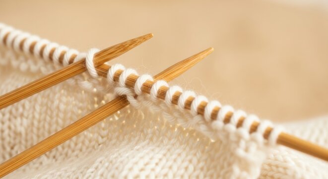 Close up view of wooden knitting needles and white yarn forming a knit pattern on a beige background showing the texture and detail of the craft