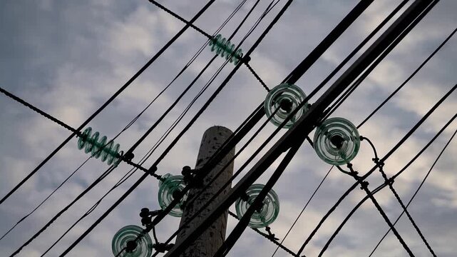 Electric utility poles and wires against a cloudy sky at dusk in an urban area