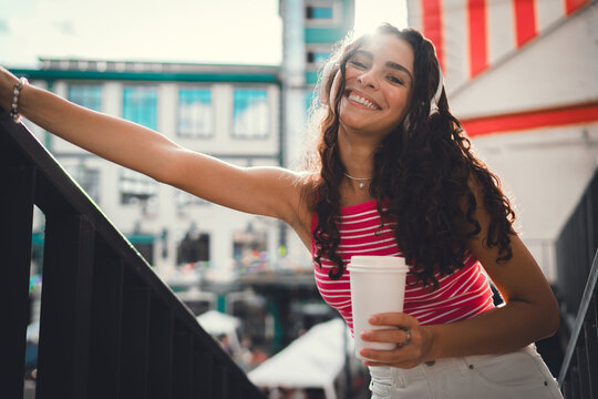 Woman smiles gently, holding coffee with both hands, wearing headphones. Image radiates warmth, simplicity and calm digital presence amid everyday tech integration.