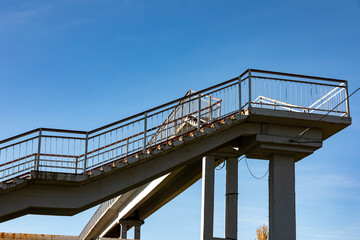 Elevated pedestrian bridge with metal railings under a clear blue sky, offering a modern urban perspective and strong geometric lines.