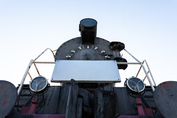 Low angle shot of an old black steam locomotive front with blank nameplate, set against a clear blue sky. Industrial and retro transportation concept.