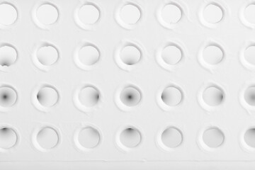 Minimalist close-up of a white surface with evenly spaced circular holes, ideal for backgrounds, design templates, or abstract concepts.