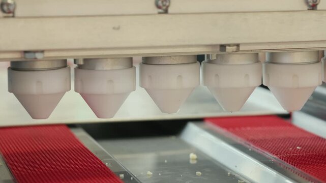 Close-up of an automated dough dispensing machine releasing evenly sized portions onto a baking tray. The precision equipment ensures uniformity in dough output for efficient baking.