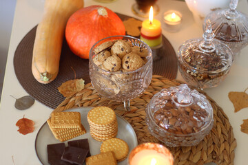Lit candles, cookies, chocolate, nuts, tea, wine, pumpkins, books, reading glasses and autumn leaves on the table. Autumnal hygge at home. Selective focus.