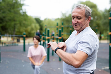 Elderly man looking at his smart bracelet in open-air sports area