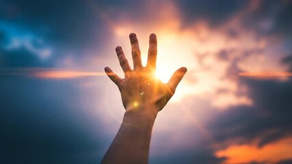 A hand reaching towards the bright sunlight amidst dramatic clouds.