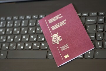 Belgium passport lies on black laptop keyboard buttons background close up. Technologies and...