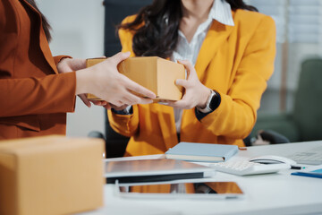 Asian female entrepreneurs coordinating product handover at an e-commerce office, preparing parcels for shipping logistics while collaborating professionally to manage online business operations