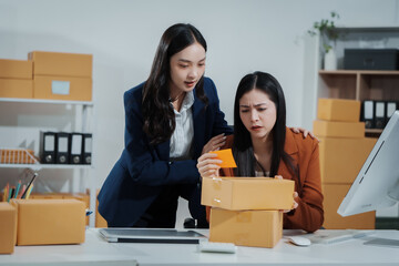 Two young Asian business woman stressed over poor sales, struggling with e-commerce order management, inventory, and logistics issues, showing visible frustration and pressure while handling parcels