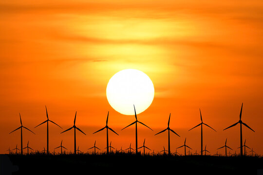 Silhouette of wind turbines at sunset with a vivid orange sky  - Powered by Adobe