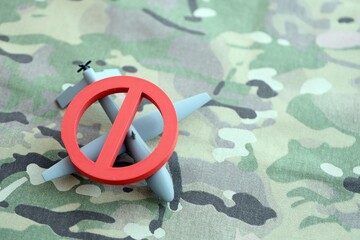Unnamed grey toy drone model and red prohibition sign on camouflage fabric close up. Anti-aircraft...