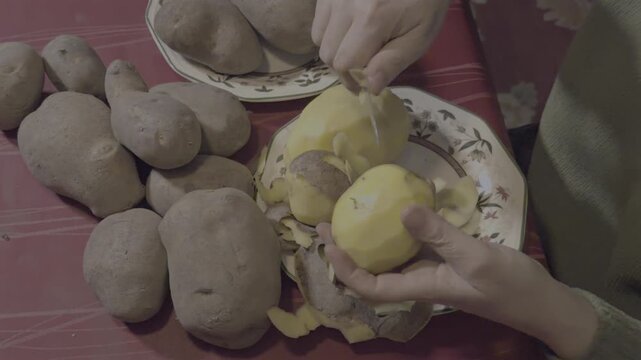 Woman's hands peeling fresh potatoes with a knife