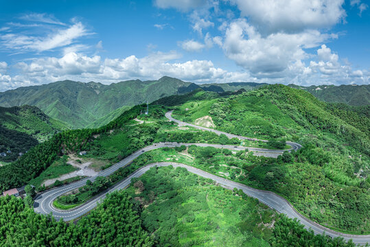 Winding asphalt road on green mountain ridges under blue sky and clouds.