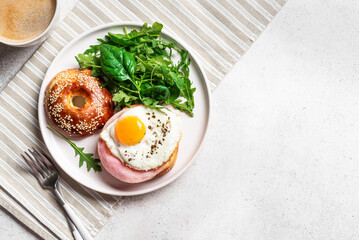 Healthy breakfast. Bagel with fried egg, ham and greens