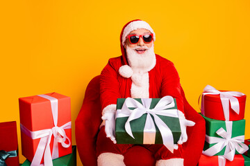 Santa in red suit with white beard sits among colorful wrapped gifts and bright backdrop delivering festive cheer and holiday shopping vibe
