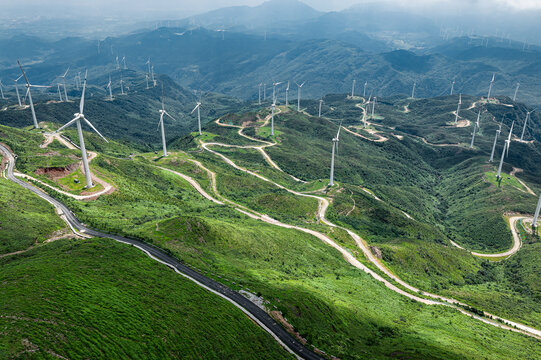 Aerial view of winding mountain road and wind farm generating electricity in green nature.