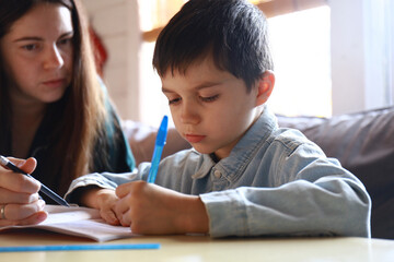 mom is doing her homework with her child. The boy is learning to write letters
