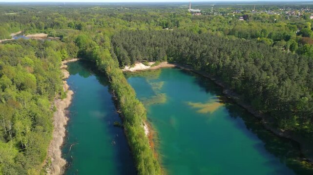 Two clear turquoise lakes lie nestled between dense forest areas, creating a calm and natural panorama under bright sunlight.