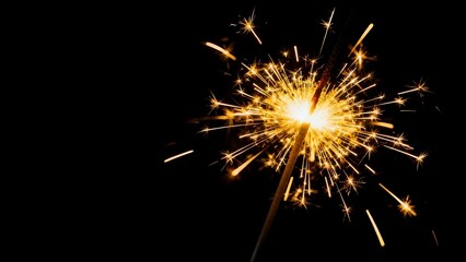Obraz premium A bright sparkling sparkler with golden sparks on a dark background. Symbol of New Year's Eve celebration, party, and fun night.