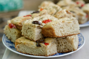 Focaccia squares piled on a plate, featuring olives, rosemary, and cherry tomatoes.