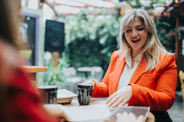 A stylish woman in an orange blazer sits at a cafe table near a bookstore, smiling as she chats with a friend over coffee. Warm, candid and social moment.