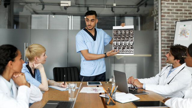 Arabic young man doctor showing his colleagues MRI scan, multiracial team of professional docotrs attending medical conference or having breefing, discussing medical cases, copy space - Powered by Adobe