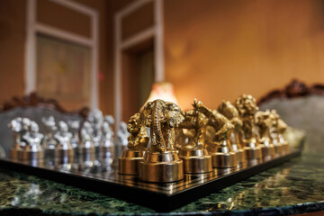 A luxury chess set shows elephant, lion, and gorilla pieces in focus on green marble. Warm lamplight reflects on metal, shallow depth of field softens the far ranks.