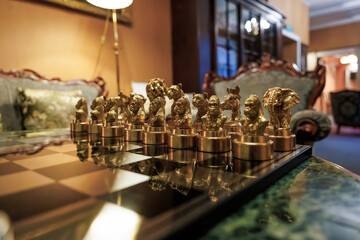 Gold animal head chess pieces sit in starting rows on a marble table in a vintage lounge, warm lamplight reflects, shallow depth and low angle emphasize texture.