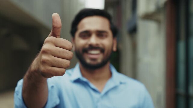 Portrait of Indian man gives thumbs up and down and stands on city street closeup. Bearded Hindu guy changes opinion from like to dislike gesturing on urban backdrop slow motion