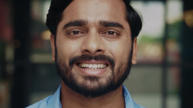Portrait of young Indian man shows toothy smile turning head to camera on street closeup. Happy Hindu male radiates positive emotions with facial expression on urban backdrop