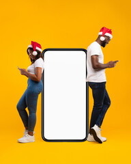 An African American couple is joyfully texting on their cellphones while wearing Santa hats.
