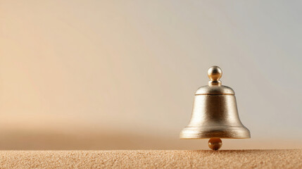 A gold bell balanced on a tiny ball, with sand beneath it and an out-of-focus background of warm colors