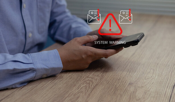 Person holding smartphone with digital system warning alert displayed above the device,Concept of cybersecurity risk, mobile malware threat, data breach notification, email security warning message