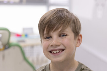 Smiling schoolboy with healthy teeth posing in bright pediatric dental clinic interior.