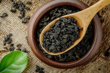 A close-up of a wooden spoon filled with black tea leaves, set against a rustic burlap background.