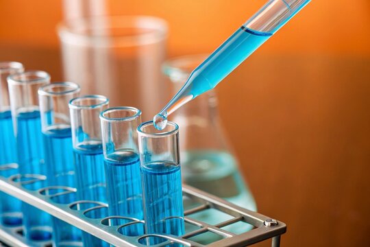 Blue liquid drips into a test tube as laboratory tools, glassware, and sterile equipment support scientific research, biotechnology testing, medical analysis, pharmaceutical experiments.