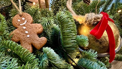 Gingerbread man cookie ornament hanging among lush green pine branches and a golden bell with red ribbon, creating a festive holiday atmosphere for seasonal celebrations. Christmas banner