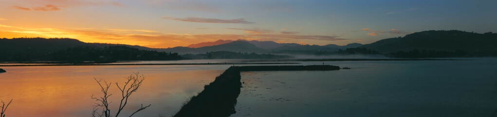 Asturias Calm lake at sunrise with soft mist rising over distant mountains and warm colors reflecting on the still water creating a serene landscape