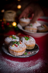 mixed fruit cupcakes dusted with powdered sugar, styled on a festive table for the Christmas and New Year holiday season. The cupcakes are topped with colorful candied fruits and arranged on a rustic 