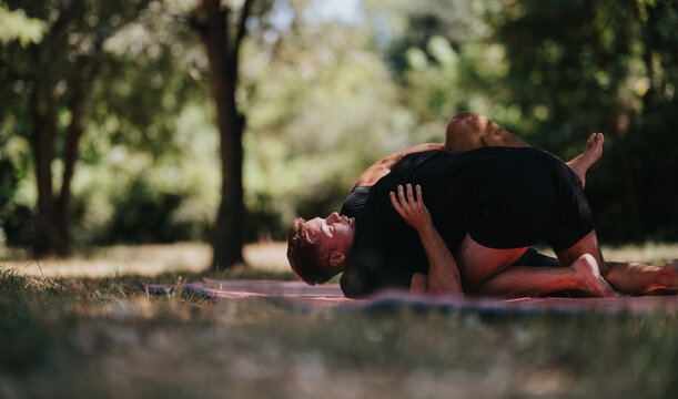 Two athletes wrestle on a mat laid in a sunny park, showcasing raw strength, focus, and athleticism in an outdoor setting.
