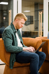Fototapeta premium Young man concentrating typing on laptop in casual office