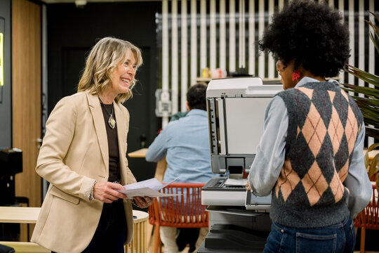 Women coworkers smiling while printing documents at office