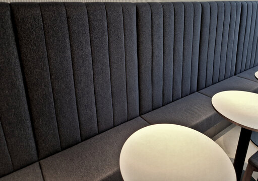 comfortable bench seat along the wall with high padded lining. upholstered in soft foam with textile cover. wooden chairs and a round table in a cafe. custom-made for the space